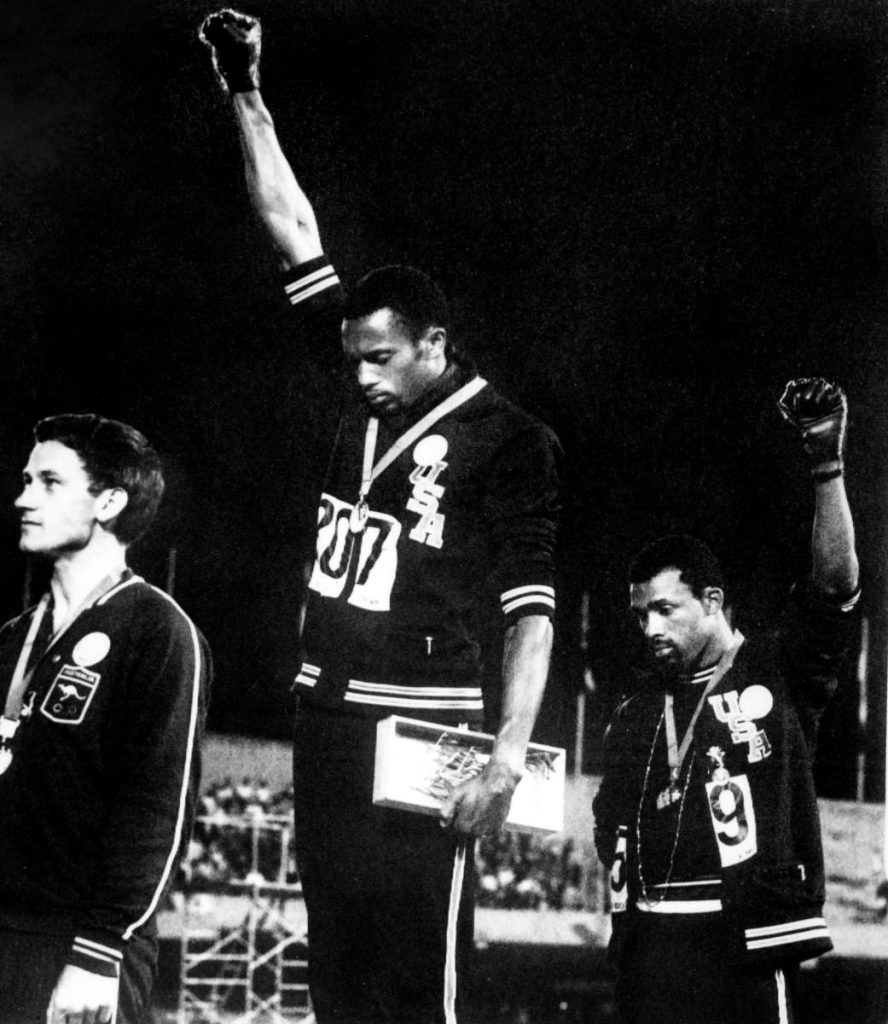 In this October 16, 1968 file photo, US athletes Tommie Smith (C) and John Carlos (R) raise their gloved fists in the Black Power salute to express their opposition to racism in the USA during the US national anthem, after receiving their medal for first and third place in the men’s 200m event at the Mexico Olympic Games. At left is Peter Norman of Australia who took second place. AFP PHOTO - - In this October 16, 1968 file photo, US athletes Tommie Smith (C) and John Carlos (R) raise their gloved fists in the Black Power salute to express their opposition to racism in the USA during the US national anthem, after receiving their medal for first and third place in the men’s 200m event at the Mexico Olympic Games. At left is Peter Norman of Australia who took second place. AFP PHOTO - -