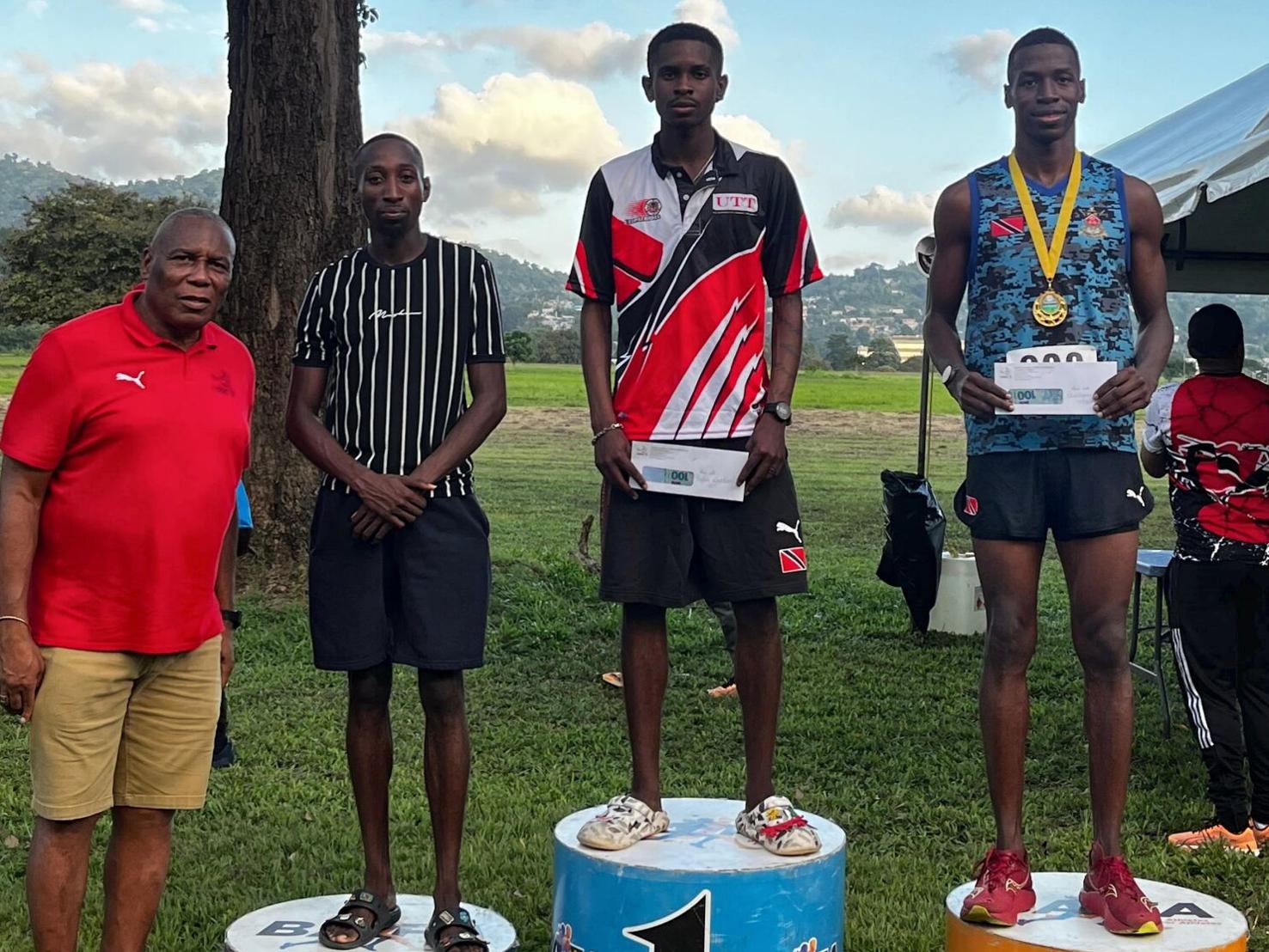 PODIUM PLACINGS: Tafari Waldron, second from right, stands at the top of the podium after receiving his NAAATT National Cross Country Championship men’s 8K winner’s prize from NAAATT president Ephraim Serrette, left, at the Queen’s Park Savannah, yesterday. Christopher Mitchell, right, finished second, with third spot going to Donnell Francis, second from left. —Photo: TESSICA LAURENCE (Image obtained at trinidadexpress.com)