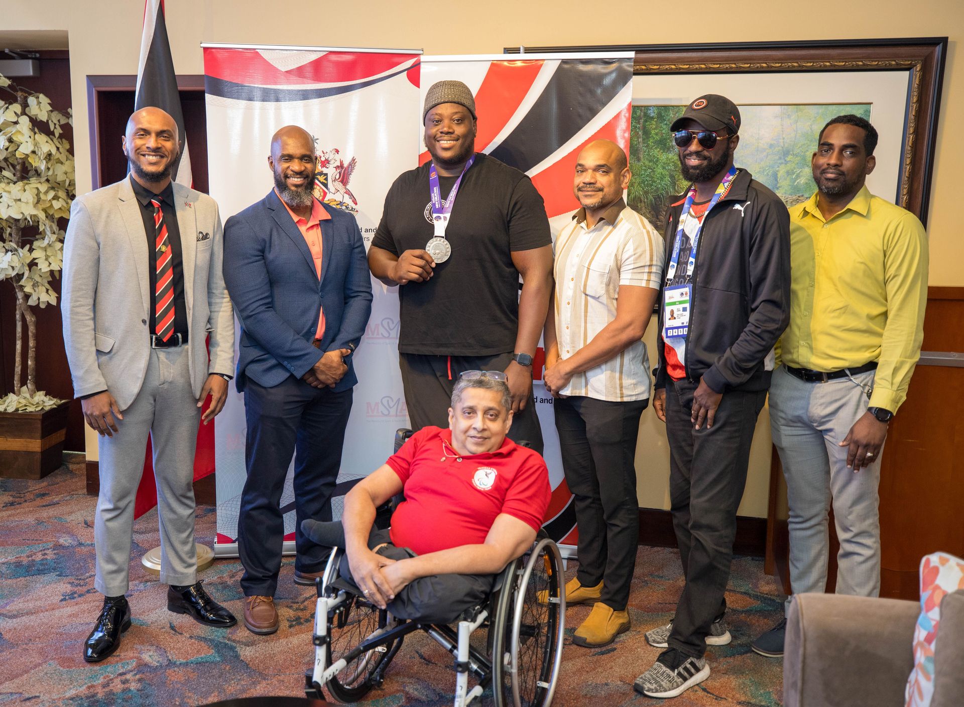 Para-Athlete Akeem “The Titan” Stewart, third from left, shows off his 2025 World Para-Athletics Championships silver medal on his arrival at the Piarco International Airport, on Monday, alongside technical administrator MSYA Rixon Powder, from left, acting permanent secretary Gabre Jesu McTair, acting assistant director Ronson Hackshaw, Paralympic Committee team lead Mickey Ruben, and SporTT communications manager Kern De Freitas and president of the Paralympic Committee Sudhir Ramessar, centre front.  Courtesy Savory Photography (Image obtained at guardian.co.tt)